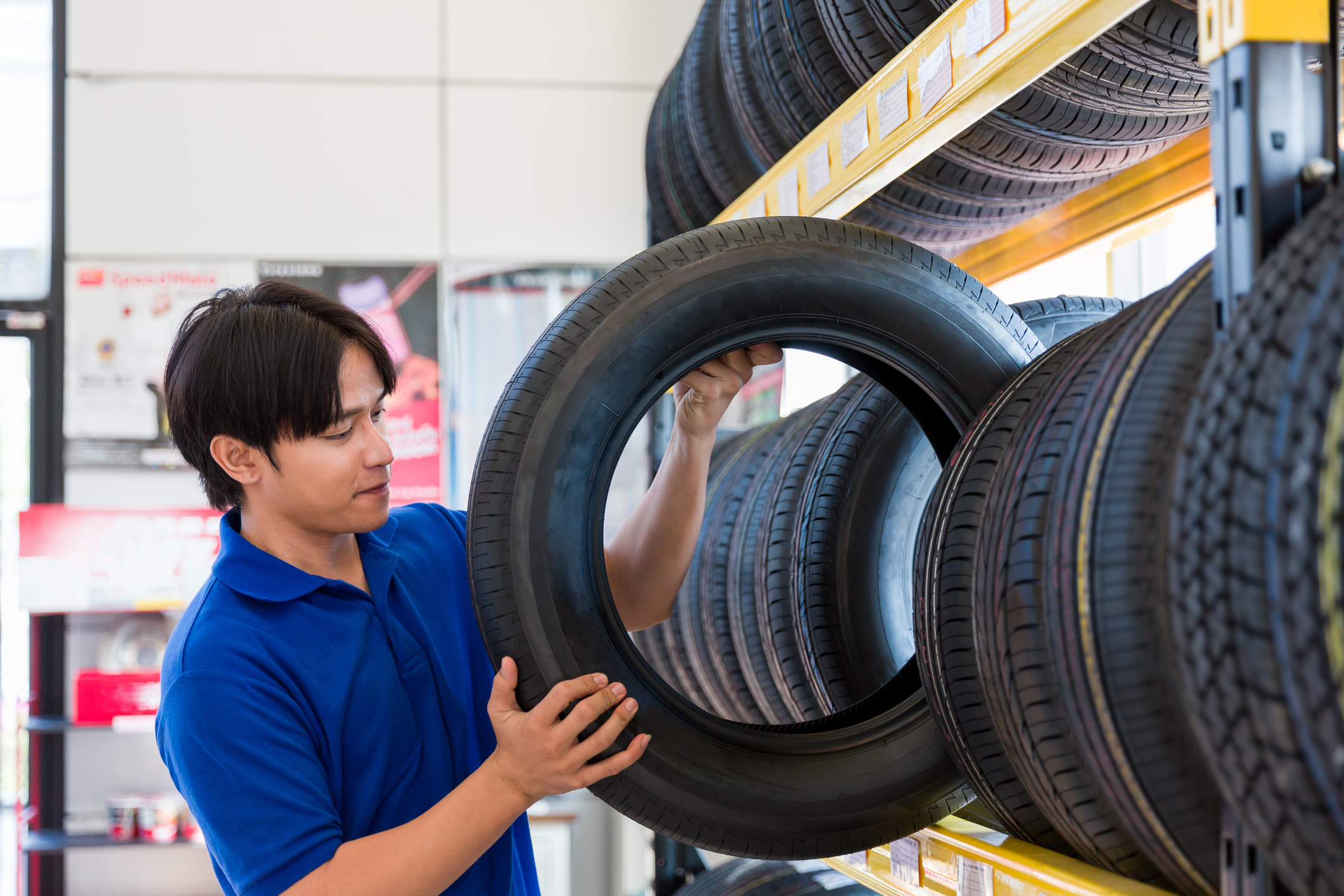 Asian male technician worker checking new tire wheel on shelves shelf at wheel store.